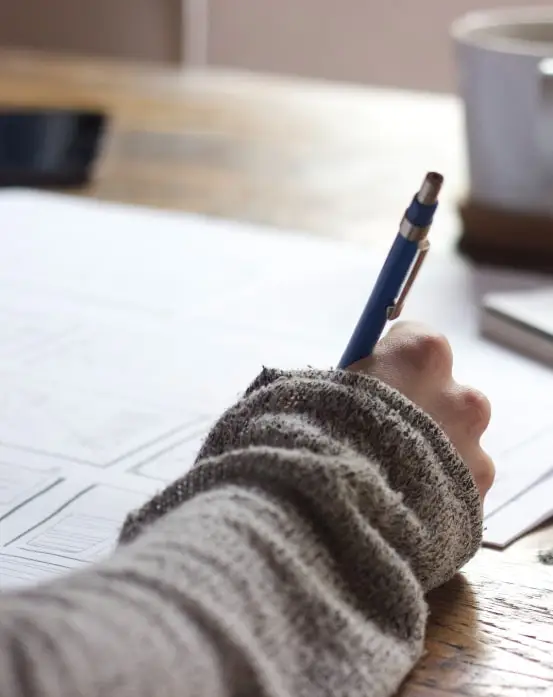 A person's hand with a pen is actively writing and editing notes on a piece of paper. The Novel View's Resources page image.