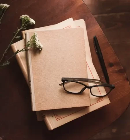 A wooden table displays books, a pen, glasses, and a notebook, creating a cozy writer's workspace. The Novel View's Story Consultation Services image